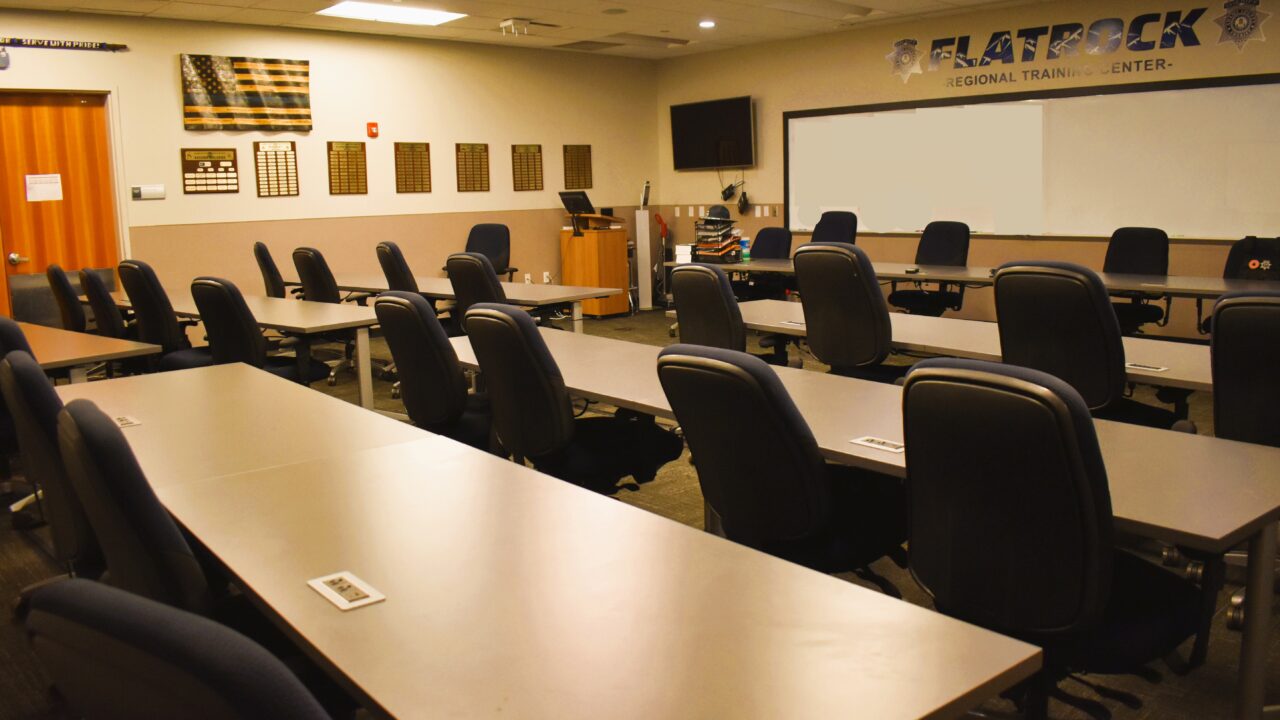 Empty training room with long tables and chairs, displaying a distressed U.S. flag and plaques on the wall.