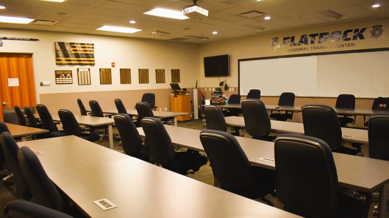 Empty training room with long tables and chairs, displaying a distressed U.S. flag and plaques on the wall.