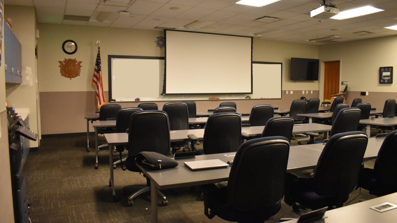 Empty classroom with rows of chairs, projector, and American flag