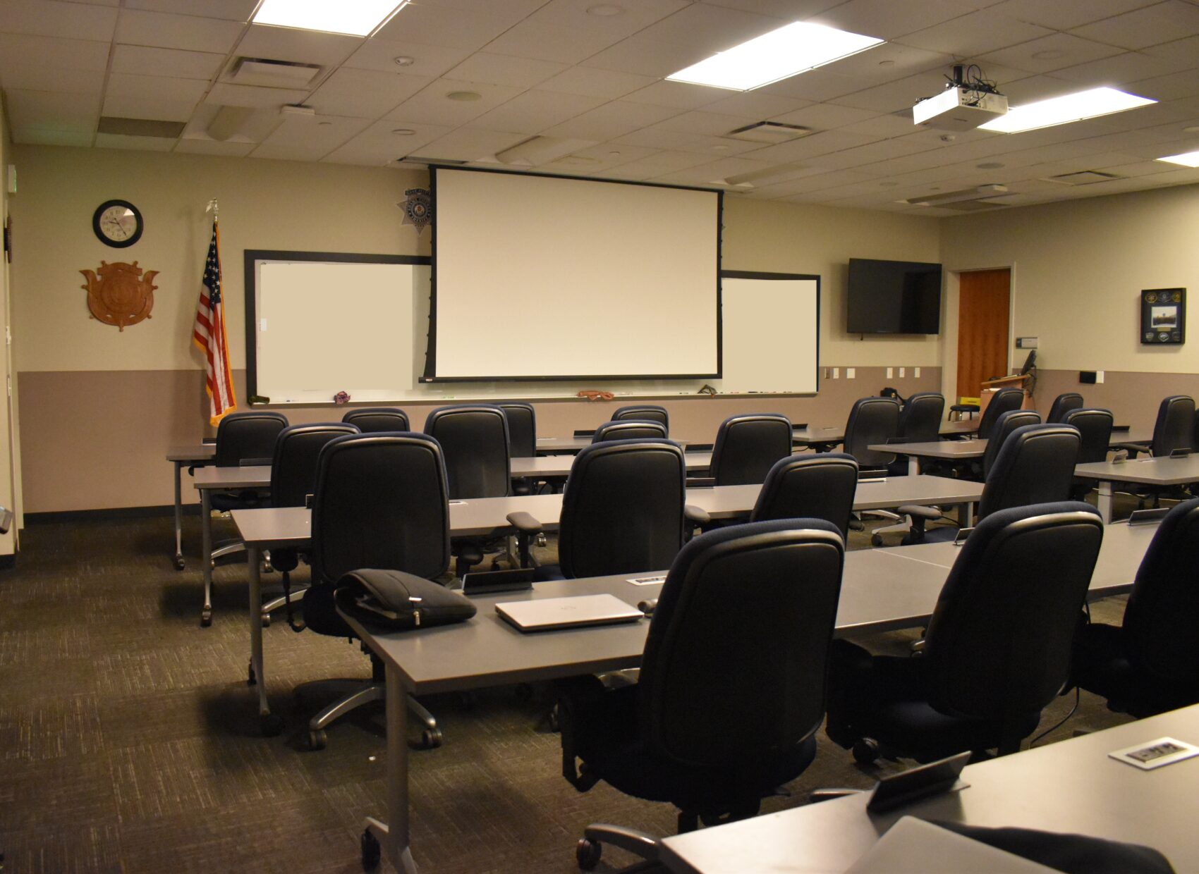 Empty classroom with rows of chairs, projector, and American flag