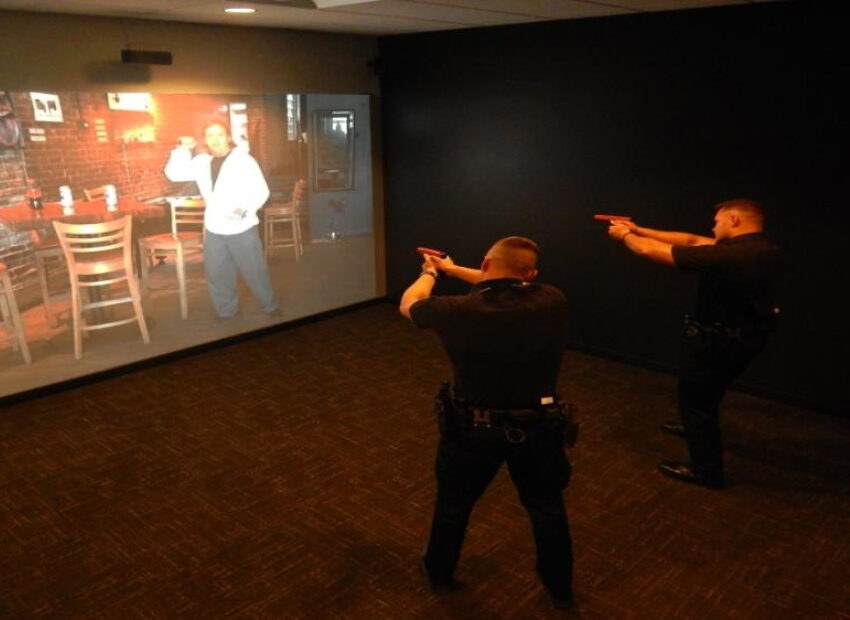 Two officers aim training pistols at a projected scenario on a wall.